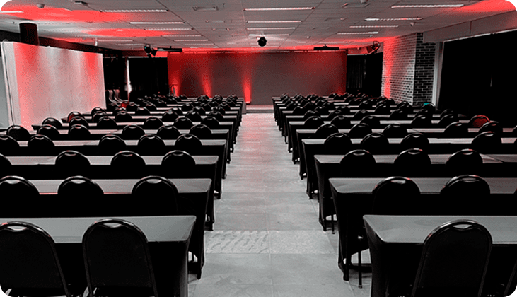 imagem do espaço gênesis, um telão de led com luzes vermelhas, cadeiras e mesas de auditório