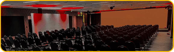 imagem do espaço gênesis, um telão de led com luzes vermelhas, cadeiras de auditório