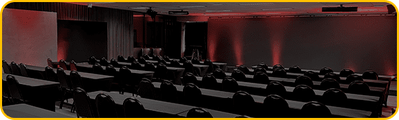 imagem do espaço gênesis, um telão de led com luzes vermelhas, cadeiras e mesas de auditório