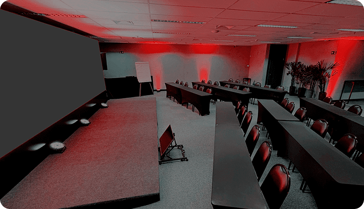 imagem do espaço gênesis, um telão de led com luzes vermelhas, cadeiras e mesas de auditório